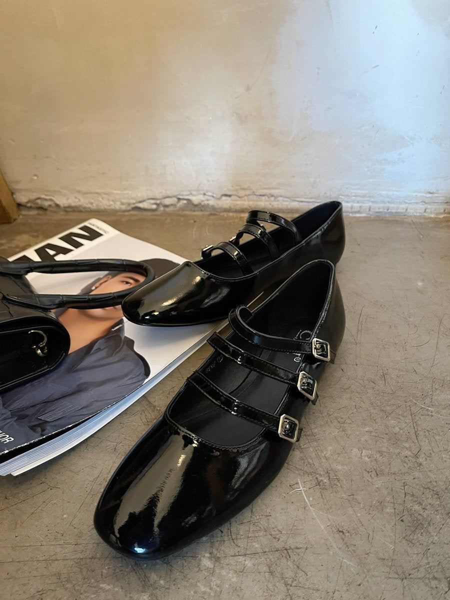 Pair of black strappy flat shoes with three buckle straps and glossy finish