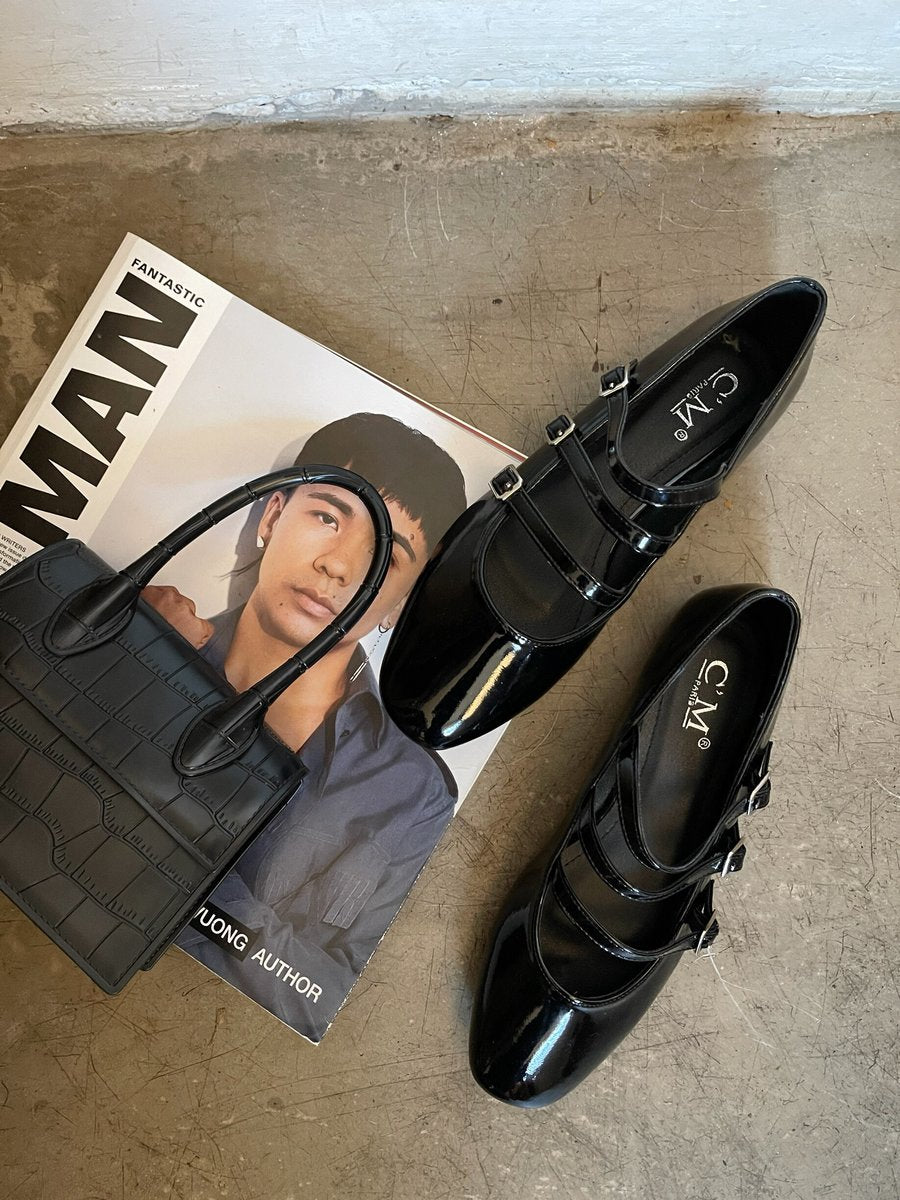 Black strappy flat shoes with buckle straps and glossy finish, shown as a pair