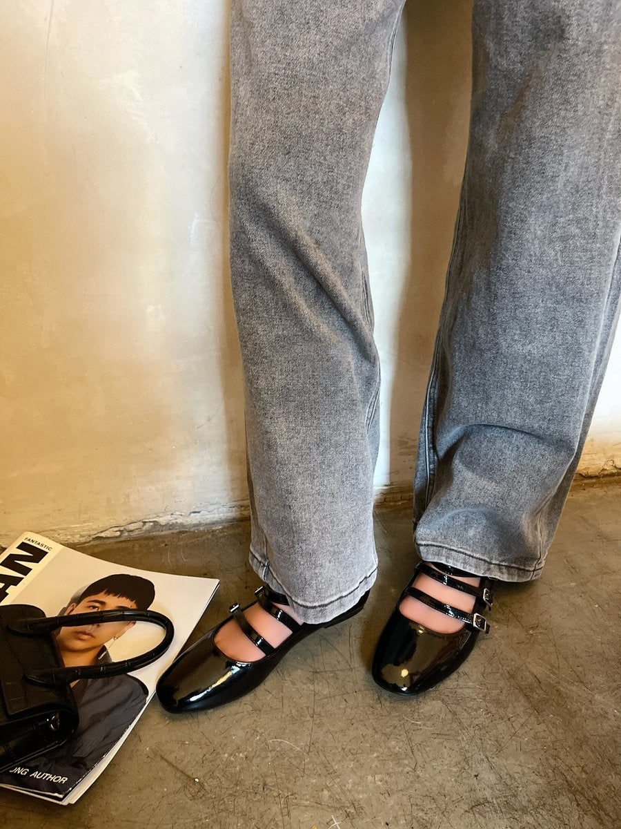 Black strappy flat shoes with buckle ankle straps and glossy finish, on model