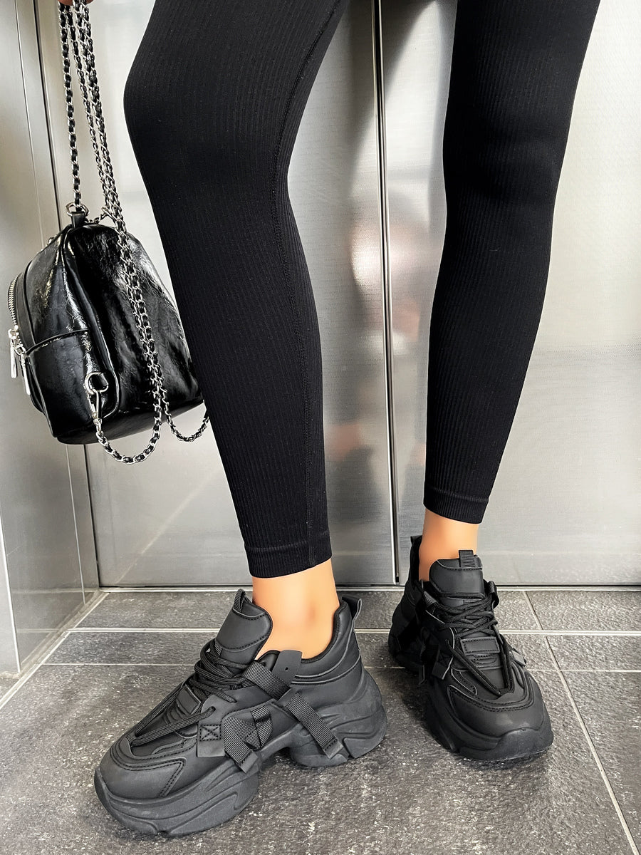 Black platform lace-up chunky trainers on legs, with lace-up front and straps
