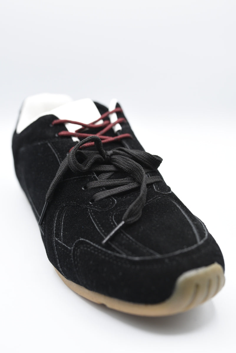 Black lace-up flat trainers with red contrast laces and tan rubber sole.