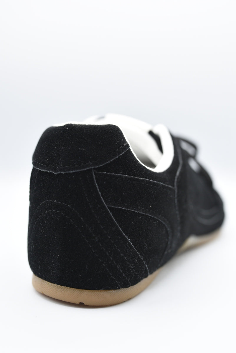 Black lace-up flat trainers, white heel lining, tan rubber sole.