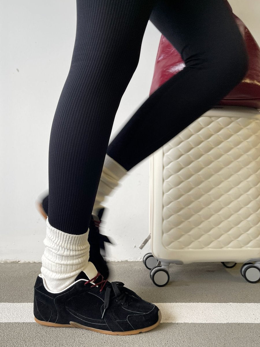 Black lace-up flat trainers with red laces, shown with standing legs