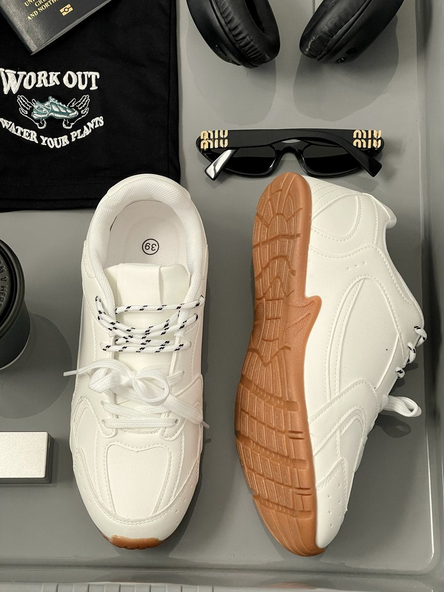 White lace-up flat trainers with tan rubber soles and cushioned tongue.