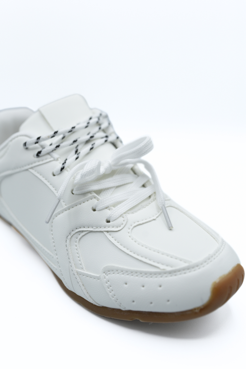 White lace-up flat trainers close-up with textured toe, stitched overlays, brown sole.